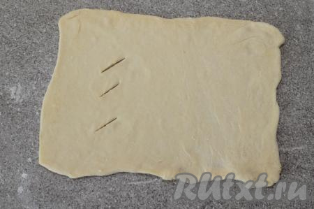 На слегка присыпанной мукой поверхности раскатать вначале одну часть теста в прямоугольник, ориентировочно, толщиной 2 миллиметра. На одной из сторон прямоугольника сделать острым ножом 3-4 разреза.