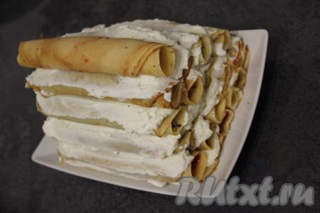 Далее продолжаем формировать блинный торт в виде избы, выкладывая в каждом последующем ряду на один рулетик меньше. Каждый слой нужно хорошо промазывать кремом. В итоге у нас получится пирамидка, как на фото.