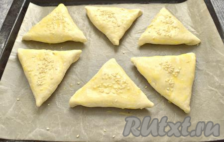 Сформированную самсу с начинкой из творога и сыра выкладываем швом вниз на противень, застеленный пергаментной бумагой. Желток слегка взбиваем вилкой и смазываем им самсу из слоёного теста. Сверху, по желанию, посыпаем заготовки кунжутом.