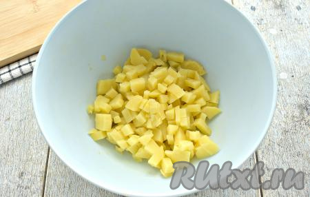 Заранее для салата отвариваем прямо в кожуре картошку и морковку (примерно, в течение 25 минут после закипания воды), затем даём им остыть, вынув из воды, в которой они варились. Яйца тоже отвариваем (варим их минут 10 после закипания), после этого заливаем их холодной водой, а после остывания очищаем. Теперь можно приступать к приготовлению салата, для этого очищаем отваренный картофель, нарезаем его на маленькие кубики и перекладываем в достаточно глубокую миску.