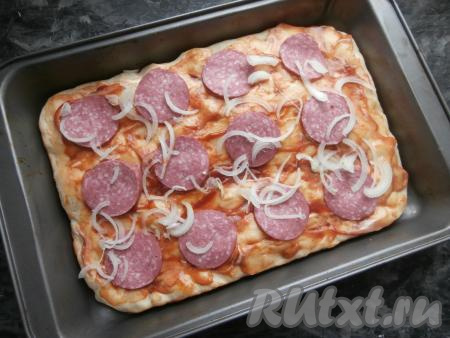 Теперь смазать тесто кетчупом, смешанным с майонезом, выложить кружочки колбасы и тонкие перья репчатого лука.