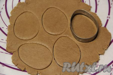 По истечении часа на слегка припылённой мукой поверхности пряничное медовое тесто раскатать в пласт толщиной, примерно, 0,5 сантиметра и с помощью вырубки для печенья вырезать пряники в виде яйца. Если нет вырубки, то вырежьте пряники острым ножом.