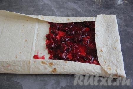 Подвернуть три края лаваша, как на фото, а затем свернуть лаваш в плоский рулет, начиная с узкой стороны с начинкой.