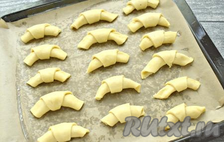 Начиная с широкой стороны, сворачиваем каждую треугольную заготовку в рогалик и выкладываем на противень "хвостиком" вниз. Я предварительно застелила противень пергаментом и смазала его немного сливочным маслом. Всего у меня получилось 24 песочных рогалика с повидлом, я пекла их в два захода.