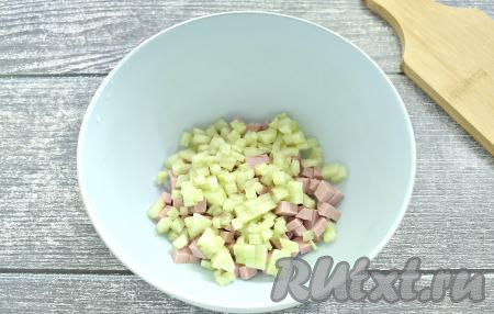Свежий огурец, по желанию, очищаем от кожуры, затем тоже нарезаем его на маленькие кубики, выкладываем к колбасе.
