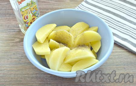 Нарезаем на крупные ломтики очищенные картошины, перекладываем в отдельную миску, по вкусу солим, приправляем специями (я посыпала чёрным молотым перцем). Добавляем пропущенный через пресс чеснок. Вливаем растительное масло. Хорошо перемешиваем картошку со специями и маслом.