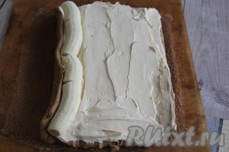 2 банана очистить, отрезать с двух сторон узкие части. Выложить бананы на край широкой стороны бисквитного коржа.