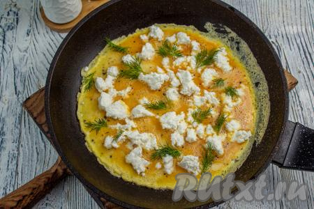 Снимите сковороду с плиты, верх омлета должен быть ещё слегка жидким. Раскрошите сыр "Рикотта", равномерно распределяя его по поверхности омлета, разложите веточки (или мелко нарезанную зелень) укропа. Сковороду накройте крышкой, верните её на плиту и готовьте омлет на минимальном огне.&nbsp;