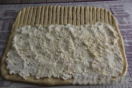 Отступив от одного длинного края 10 сантиметров, выложить творожную начинку на тесто, распределяя её тонким, ровным слоем. С остальных трёх краёв теста, выкладывая начинку, следует отступать по 1 сантиметру от края. 10 сантиметров теста, оставшиеся без начинки, нарезать на полоски шириной 1-1,5 сантиметра, как на фото.