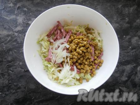 В миску с капустой и колбасой выложить отжатый лук и консервированный горошек.