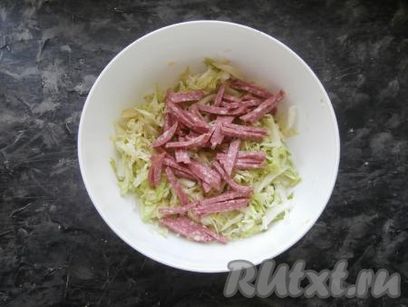 Капусту нарезать тонко, посолить, выложить в миску. В этот раз я готовила салат "Днестр" с молодой капустой, поэтому только слегка помяла её руками. Если же вы готовите этот салат с зимними сортами капусты, тогда тонко нарезанную капусту нужно хорошо помять руками, чтобы оно дала сок и стала более сочной. К капусте добавить нарезанную соломкой копчёную колбасу.