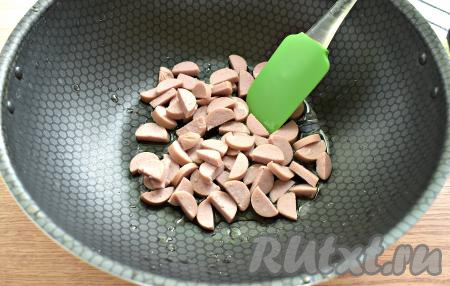 Разогреваем в сковороде растительное масло, затем выкладываем нарезанные сосиски, обжариваем их на среднем огне 2-3 минуты, помешивая.