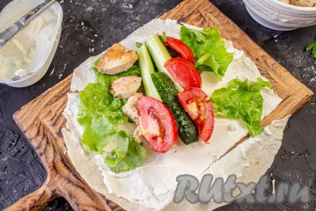 Ближе к одному краю круга из лаваша выложите лист салата, часть помидоров и огурцов, несколько кусочков обжаренного куриного мяса. Выкладывая овощи и кусочки курицы, учитывайте, что мы будем формировать 4 ролла.
