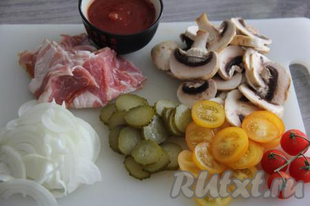 Подготовить начинку для пиццы, для этого очищенный лук нужно нарезать на тонкие полукольца. Вымытые помидоры нарезать на кружочки (помидоры черри можно просто разрезать пополам). Бекон (или любые колбасные изделия) нарезать на тонкие кусочки. Шампиньоны промыть, обсушить и нарезать их на пластины. Огурчик нарезать на кружочки. 