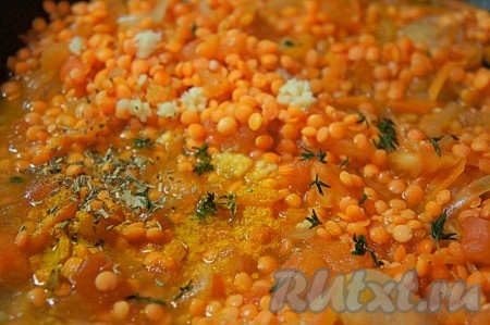 Чеснок пропустить через пресс и добавить к чечевице, добавить зелень тимьяна, сушеный розмарин, куркуму, чёрный перец, перемешать. Тушить ещё 5-7 минут на медленном огне.