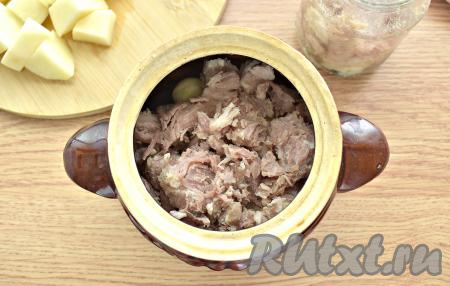 Тушёнку выкладываем в тарелку, разминаем вилкой на небольшие кусочки, а затем перекладываем её в горшочек.