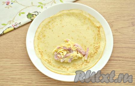 Параллельно с жаркой блинчиков приступаем к фаршировке. Выкладываем на блин столовую ложку начинки из ветчины и сыра, подворачиваем боковые края блинчика с двух сторон на начинку, а затем, сворачиваем блин в рулетик, начиная со стороны с начинкой.