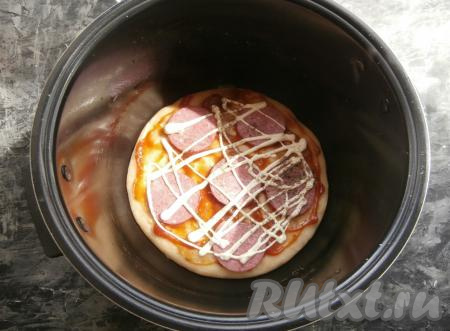 Готовить основу пиццы на режиме "Выпечка" 15 минут, затем крышку мультиварки открыть. Основу пиццы смазать сверху кетчупом, выложить кружочки колбасы, смазать немного майонезом, поперчить.