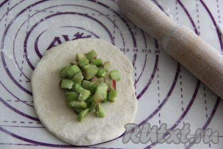 Подошедшее дрожжевое тесто обмять, разделить его на 8 частей (я дополнительно небольшой кусочек отщипнула для украшения пирожков). На присыпанной мукой поверхности скалкой каждую часть теста раскатать в круг. Начинку тоже разделить на 8 частей. Выложить часть начинки из ревеня на середину раскатанного теста.