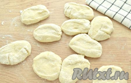 Поднявшееся дрожжевое тесто обминаем. Делим на 12 равных кусочков. Каждый кусочек теста прижимаем ладонью на припылённой мукой поверхности.