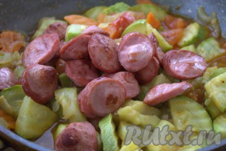 Далее в сковороду к овощам добавить уже обжаренные сосиски, перемешать и продолжить тушить, не закрывая крышку, 2-3 минуты.