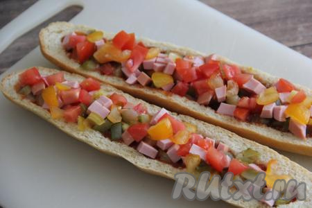 В отдельной миске смешать нарезанные огурцы, колбасу и помидоры, а затем выложить на смазанные кетчупом (или томатным соусом) багеты, заполняя хлебную лодочку.&nbsp;