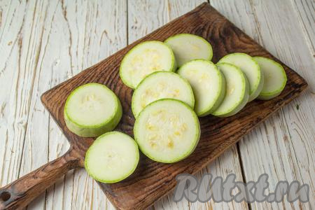 Зубчики чеснока очистите. Помидор вымойте. Для этого блюда нужно брать молодой кабачок с мелкими семечками (если кожица у кабачка жестковата, тогда лучше её срезать). Нарежьте кабачок на кружочки толщиной 1,5-2 сантиметра. Выложите кабачки в один слой в форму для запекания (или на противень).&nbsp;