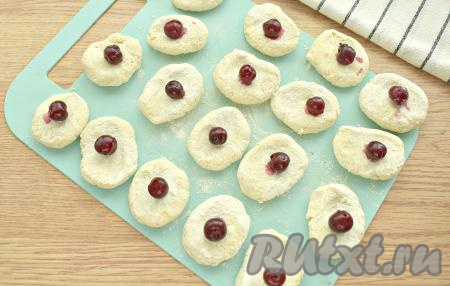 Кусочки обваливаем в муке, прижимаем, формируя лепёшку. На каждую лепёшку кладём по ягодке вишни.