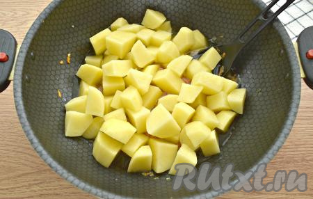 Картошины очищаем, нарезаем их на крупные кубики, выкладываем к обжаренным овощам. Вливаем кипячёную воду, после закипания, уменьшив огонь, тушим картошку под крышкой 10 минут, иногда помешивая.