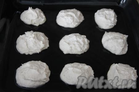 На противень влить масло, равномерно распределить. Поставить противень с маслом в разогретую до 180 градусов духовку, прогреть в течение 5 минут. Затем достать противень, прогретый с маслом, и сразу столовой ложкой, смоченной водой, выложить творожное тесто на противень, формируя круглые приморские творожанники. Выкладывать заготовки нужно на расстоянии друг от друга (у меня получилось 9 штук).