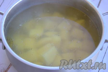 Нарезать очищенный картофель на небольшие кусочки, выложить его в кастрюлю с куриным бульоном, после закипания варить на небольшом огне минут 10 (до полуготовности картошки).