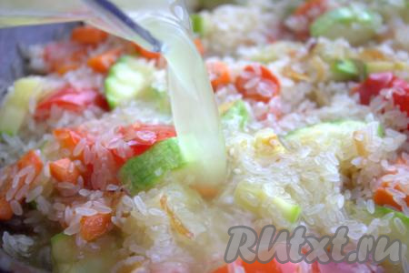 Далее в сковороду влить тёплую кипячёную воду (можно воду заменить овощным бульоном), тщательно разровнять рис с овощами.