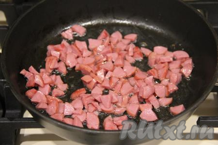 В сковороду влить немного растительного масла и выложить нарезанные сосиски. Обжарить сосиски на среднем огне, помешивая, до золотистого цвета, затем дать немного остыть.