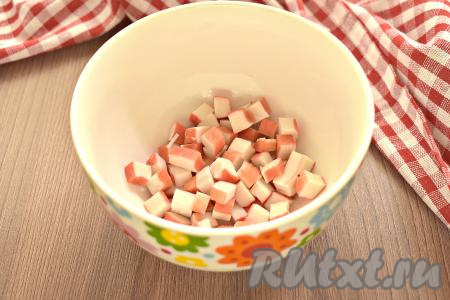 Крабовые палочки для салата должны быть разморожены, поэтому достаньте их заранее. Куриные яйца отвариваем в течение 10 минут с момента закипания воды, затем заливаем их ледяной водой, а после остывания очищаем. Извлекаем размороженные крабовые палочки из упаковки, нарезаем на небольшие кубики и перекладываем в миску.