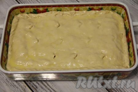 Вторую часть теста на присыпанной мукой поверхности раскатать в прямоугольный пласт, размер которого чуть больше размера формы для выпечки, переложить этот пласт теста в форму для выпечки, накрывая начинку. Края теста хорошо защипнуть со всех сторон, формируя закрытый пирог. С помощью ножниц сделать несколько надрезов на поверхности теста. Смазать верх пирога взбитым желтком.