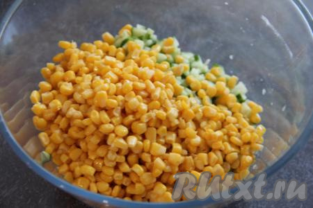 В миску с крабовыми палочками добавить нарезанный огурчик и кукурузу, предварительно слив с неё жидкость.