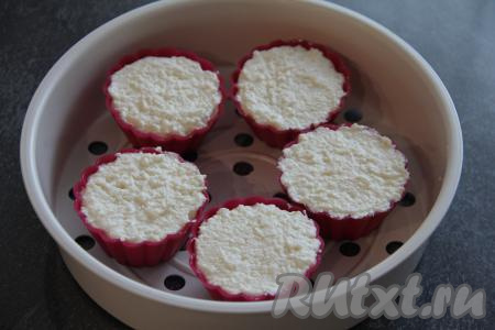 Получившуюся творожную массу разложить по силиконовым формочкам для кексов. Формы заполнять полностью. Поставить формочки с творожной массой на подставку для пароварки. В чашу мультиварки влить воду, включить мультиварку на режим "На пару", крышку закрыть, после звукового сигнала (когда вода закипит), сверху поставить подставку для пароварки с формочками, крышку мультиварки закрыть. Готовить творожную запеканку 20 минут на режиме "На пару".