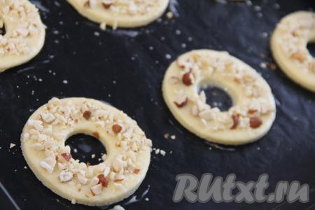 Переложить колечки на противень, застеленный ковриком для выпечки (или пергаментом). Смазать верх колечек взбитым желтком. Орехи порубить ножом и посыпать орешками песочные колечки.