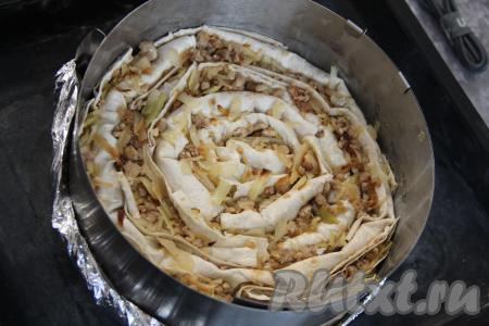 Рулетики из лаваша выкладывать в виде улитки в разъёмную форму (у меня форма диаметром 25 сантиметров без дна, поэтому дно я сделала из фольги), начиная с середины этой формы. У меня осталась часть лаваша, я его нарезала на кусочки и вставила между рулетиками. Оставшуюся начинку тоже выложила между рулетиками.