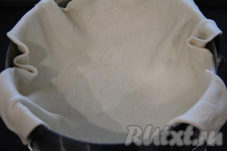 Слегка раскатать слоёное тесто на присыпанной мукой поверхности и выложить в форму для выпечки, сформировав бортик. Я выпекала в разъёмной форме диаметром 20 сантиметров и маслом её не смазывала, но, если не уверены в качестве формы, смажьте её немного маслом перед выкладыванием теста.