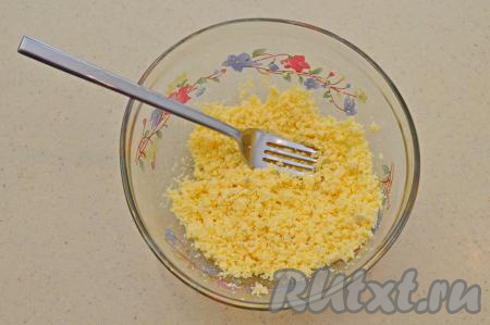 Из каждой половинки варёного яйца аккуратно вынуть желток. Все желтки поместить в небольшую пиалу и размять в мелкую крошку при помощи вилки.