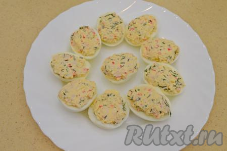Белки яиц наполнить смесью из желтков, крабовых палочек, сыра, зелени и майонеза. Начинки не жалеем и раскладываем её ещё и немного сверху. Затем начинку нужно немного прижать, как бы формируя плоскую поверхность. Это нужно, чтобы сверху в дальнейшем  на фаршированные яйца выложить украшение из моркови.