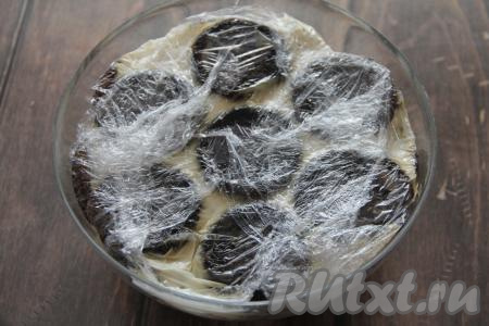 Накрыть торт свисающими краями пищевой плёнкой, слегка прижать сверху все слои. Убрать миску с тортом "Черепаха" в холодильник на ночь. Немного оставшегося сметанного крема уберите в холодильник, для того чтобы на следующий день нарисовать рот и глазки черепашки.