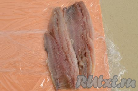 Морковь, не очищая от кожуры, сварить до готовности (на отваривание после закипания воды потребуется минут 25-30, готовая морковка будет легко прокалываться ножом), остудить полностью и очистить. Селёдку заранее разделать на филе, удалить кожу и косточки. Для этого блюда лучше всего брать не сильно солёную селёдочку. Доску застелить пищевой плёнкой. Ближе к одному краю плёнки выложить два филе "валетом" (хвосты филе смотрят в разные стороны). Филе селёдки нужно выкладывать очень близко друг к другу.