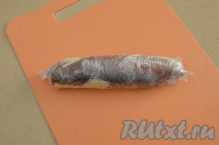 Начиная с широкой стороны, свернуть филе сельди с начинкой в плотный рулет, помогая пищевой плёнкой. Плотно завернуть получившийся рулет из сельди в пищевую плёнку. Концы плёнки скрутить, как концы конфетки. В таком виде отправить закусочный рулет в морозилку на 1 час.