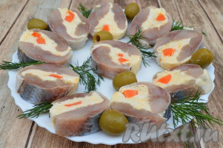 По прошествии часа рулет из сельди с творожным сыром достать из морозилки, снять пищевую плёнку, аккуратно острым ножом нарезать на кусочки и выложить на тарелку, украсить (я украсила веточками укропа и оливками) и подать к столу. Если вы готовите закуску заранее (за несколько часов до подачи), тогда можете оставить её в морозилке в пищевой плёнке, а незадолго до подачи нарезать на кусочки (чтобы подмороженная начинка разморозилась). Вкусный, просто тающий во рту, аппетитный рулет из сельди с творожным сыром станет великолепной закуской к праздничному столу.