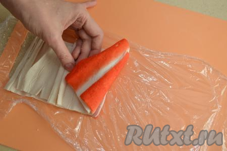 Крабовые палочки заранее разморозить и снять с них слюду. Начинаем формировать рулетики. Немного помять каждую крабовую палочку руками, после такой процедуры она будет легче разворачиваться. Развернуть крабовую палочку, выложить её на застеленную пищевой плёнкой поверхность красной стороной вниз. Следующую развёрнутую палочку постелить внахлёст на первую, сдвинув так, чтобы красная часть первой палочки следовала за красной частью второй. Сверху выложить внахлёст третью развёрнутую палочку так, чтобы красная часть палочек снаружи следовала, как практически непрерывная красная линия (на фото выложены 3 палочки, я специально показала, как они лежат).