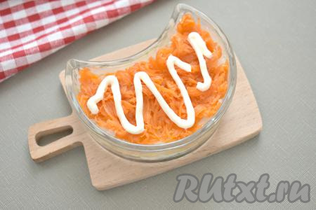 Поверх лука равномерно выкладываем натёртую на крупной тёрке морковку, смазываем майонезом.