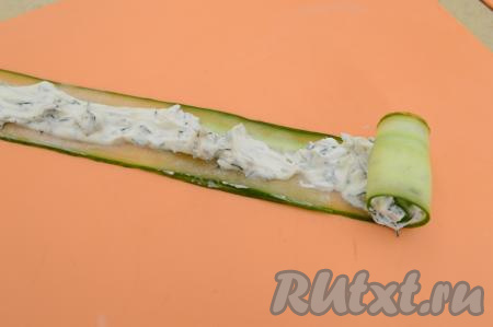 На получившуюся полоску из огурца нанести часть начинки из творожного сыра и зелени. С одного края оставить 2-3 сантиметра огурца чистым (без начинки). Скрутить полоску из огурца в плотный рулет, начиная с края с начинкой.