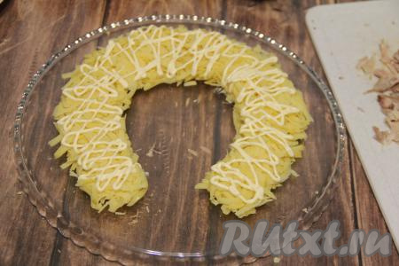 Натереть на крупной тёрке очищенный картофель. Выложить его на плоскую тарелку в виде подковы, сверху нанести сетку из майонеза, можно посолить по вкусу.